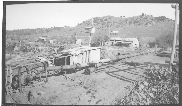 Tin shed with large pipe for sluicing next to it and house in background