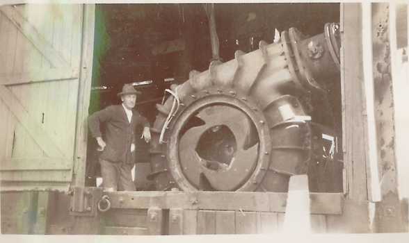 Man with hat standing next to large engine.