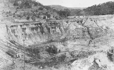 Open cut mine with pipes protruding from processing shed.