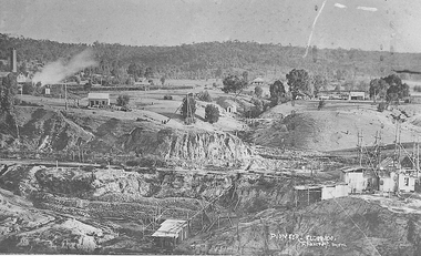 Open cut mine with barge, processing shed and wooden buildings.