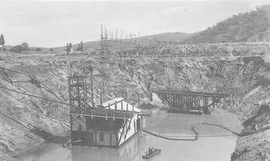 Barge, pump, and two men in dinghy in creek.