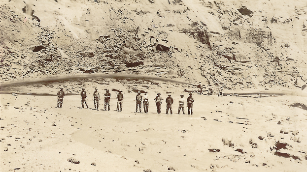 Eleven men standing under jet of water from hydraulic nozzle.