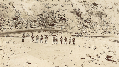 Eleven men standing under jet of water from hydraulic nozzle.