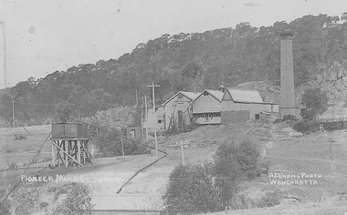 Wooden buildings with tall, brick chimney stack next to them.