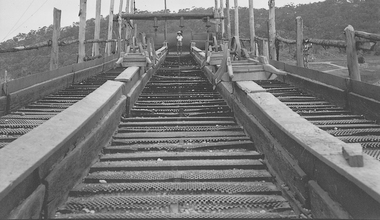 Man standing at the end of a series of riffle boards on a barge.