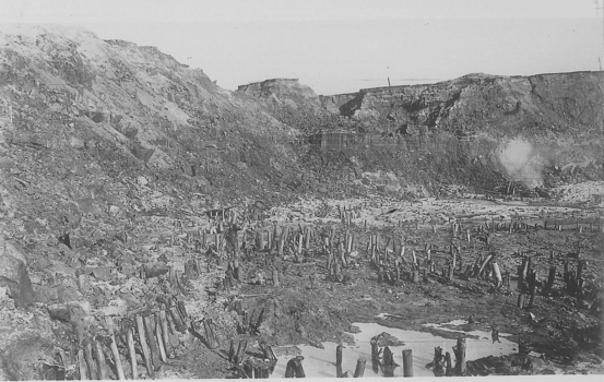 Open cut mine with short pieces of timber in ground.