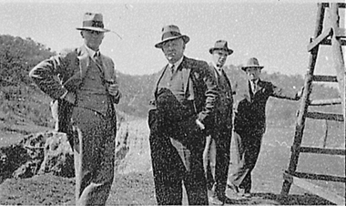 Four men standing, wearing suits and hats.