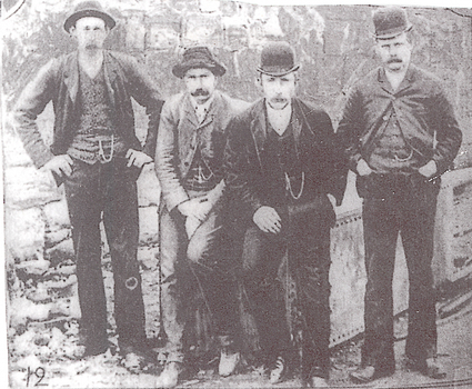 Four men dressed in trousers, jackets, waistcoats and hats posed for photo.