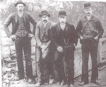 Four men dressed in trousers, jackets, waistcoats and hats posed for photo.