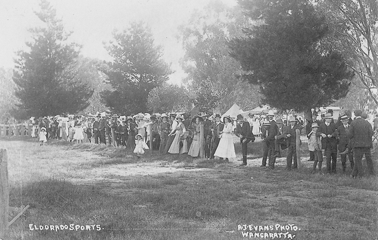 Crowd of men, women and children standing alongside a post and wire fence