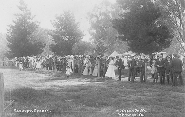 Crowd of men, women and children standing alongside a post and wire fence