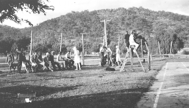 Group of men and women sitting and standing next to a tennis court. 