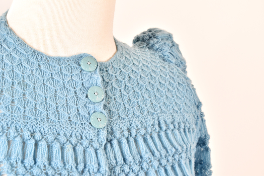 detail showing bodice and left shoulder of blue knitted children's cardigan with three blue buttons