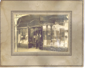 View from street of front of Miller Brothers China and Glass shop. Two men stand in the doorway.
