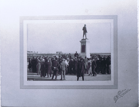 Dozens of men are standing around a statue of a man on a pedestal