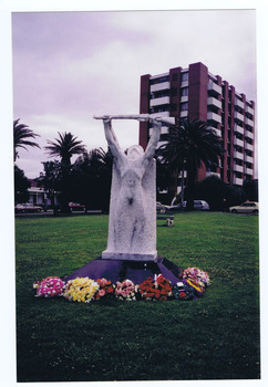 White sculpted figure of a soldier holding a rifle above his head. The statue stands on a red plinth. Eight floral wreaths are placed around the plinth.