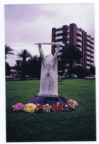 White sculpted figure of a soldier holding a rifle above his head. The statue stands on a red plinth. Eight floral wreaths are placed around the plinth.
