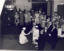 A woman in a dress curtseys in front of the Queen Mother while a large group of dignitaries looks on