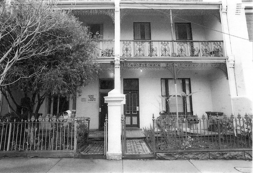 Two adjoining two-storey brick terrace buildings with wrought iron balustrades, front fences and gates. A sign next to the door on the building on the left says Sacred Heart Mission and then some indecipherable text. A second, smaller, sign is indecipherable.