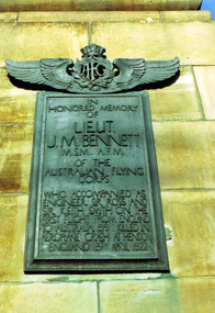 Green rectangular plaque with raised text mounted on stone. At the top of the plaque is the winged insignia of the Australian Flying Corps.