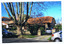 Single storey residence with brick roof. A car is in the driveway. Other cars are park in the street in front. A plaque is on a pillar at the end of the front fence, next to the driveway.