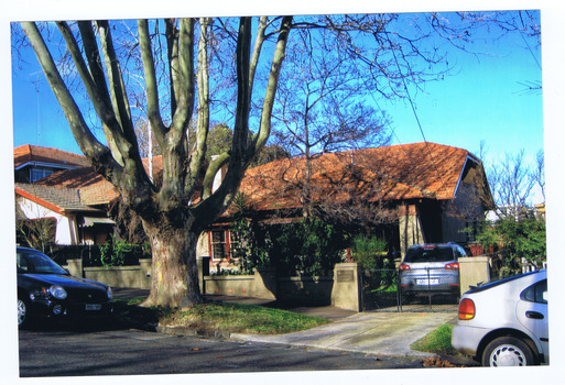 Single storey residence with brick roof. A car is in the driveway. Other cars are park in the street in front. A plaque is on a pillar at the end of the front fence, next to the driveway.