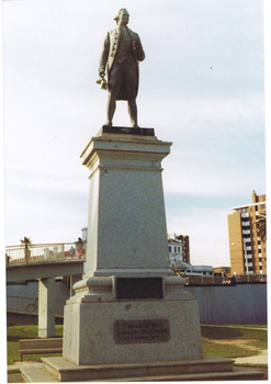 Bronze statue of man in wig, jacket, breeches and stockings standing on a granite pedestal and holding a navigational tool.