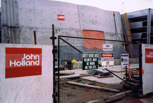 Vertical slabs of stone behind a temporary wooden fence and metal mesh gate.