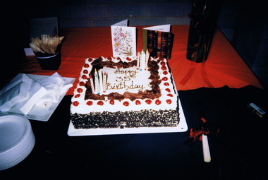 A square cake decorated with candles, icing and the words Happy 35th Birthday. Next to the cake are plates, table napkins, cutlery, two cards and a wrapped gift.