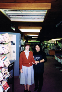 Two women stand next to shelves of books