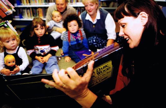 A woman holds open a book for four children and three adults to see  
