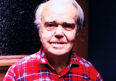 Head and shoulders of elderly man in red, white and blue plaid shirt