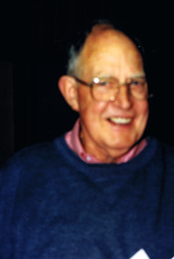Blurred image of head and shoulders of man wearing glasses, a pink shirt and blue jumper.