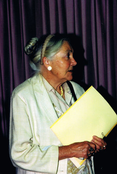 Profile of elderly woman in a light coloured jacket and holding a yellow folder