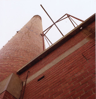 Part of a brick wall, chimney and metal structure.