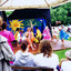 Girls in colourful costumes perform on a wooden stage, Other figures look on.