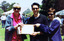 Three people standing in a park hold a framed document