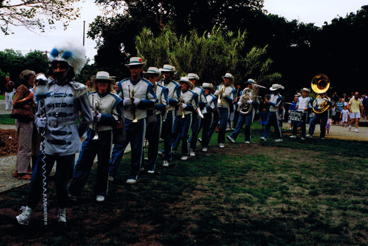 Figures in marching uniforms and holding musical instruments stand in a line