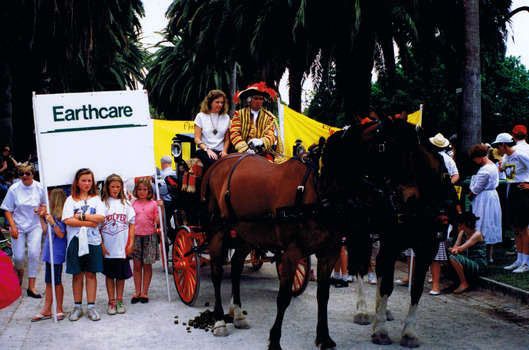 Young people stand by and hold a sign that reads "Earthcare". Next to them is a horse and carriage. Two figures sit at the front of the carriage.