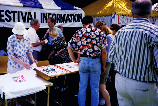 Figures look at items displayed at a gazebo that has a sign that reads "Festival Information"