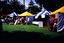 A row of colourful gazebos on a lawn. People on the lawn are visiting them.