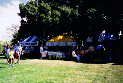 People visiting a row of gazebos in a park.