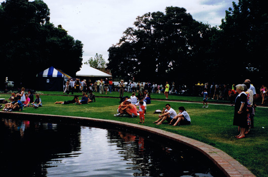 Figures sitting and standing on lawn near a pond