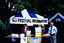 Figures stand near a gazebo that has a sign that reads "Festival Information"