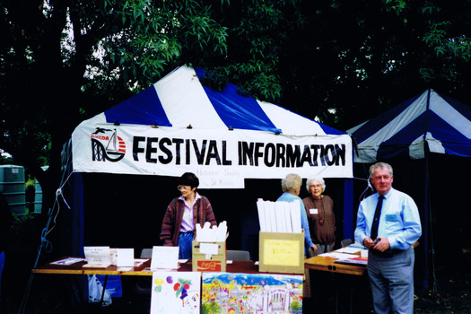Figures stand near a gazebo that has a sign that reads "Festival Information"