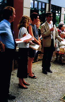 A man addresses a group of people outside a building. Three people stand next to him.