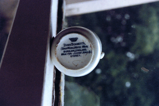 Bottom of white cup showing the image of a crown and the words "Dunn Bennett's (Gold Medal) Hotel Ware Burslem, England, Made for: J Leigh Jones & C Sydney"