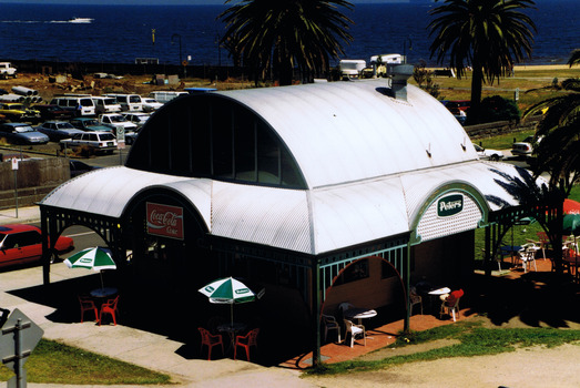 Free standing building with curved metal roof and verandah on all sides. It is in a coastal park by the water.
