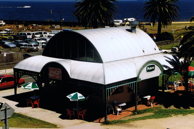 Free standing building with curved metal roof and verandah on all sides. It is in a coastal park by the water.