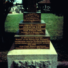 A stack of four granite blocks on a marble base. The highest block bears no inscription. The other three are engraved in gold lettering. 